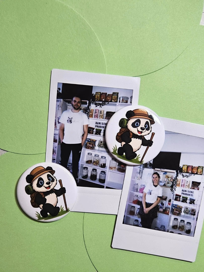 Personalisierbarer Panda-Magnet mit Wanderer-Motiv fixiert Polaroid-Fotos auf grünem Grund; zeigt die Nutzung als praktischer Fotohalter für Reiseerinnerungen und Outdoor-Abenteuer