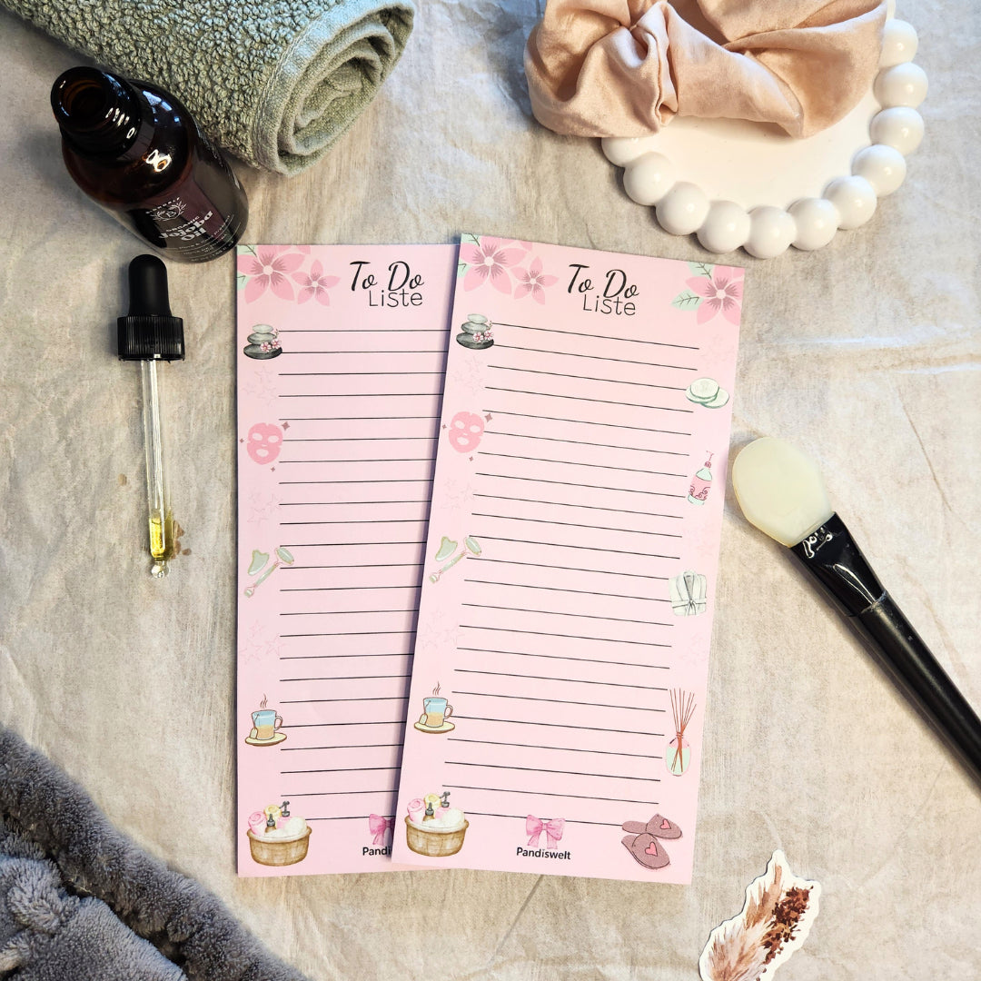 Ästhetischer To-Do-Listen Block „Spa Moment“ in Rosa von Pandiswelt für die tägliche Organisation, umgeben von Wellness-Utensilien wie Jojoba-Öl, einer Pipette und einem Handtuch auf hellem Stoffhintergrund