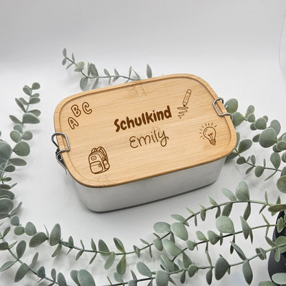 Personalisierte Brotdose aus Edelstahl mit Bambusdeckel und Namensgravur "Schulkind Emily", umgeben von Eukalyptuszweigen