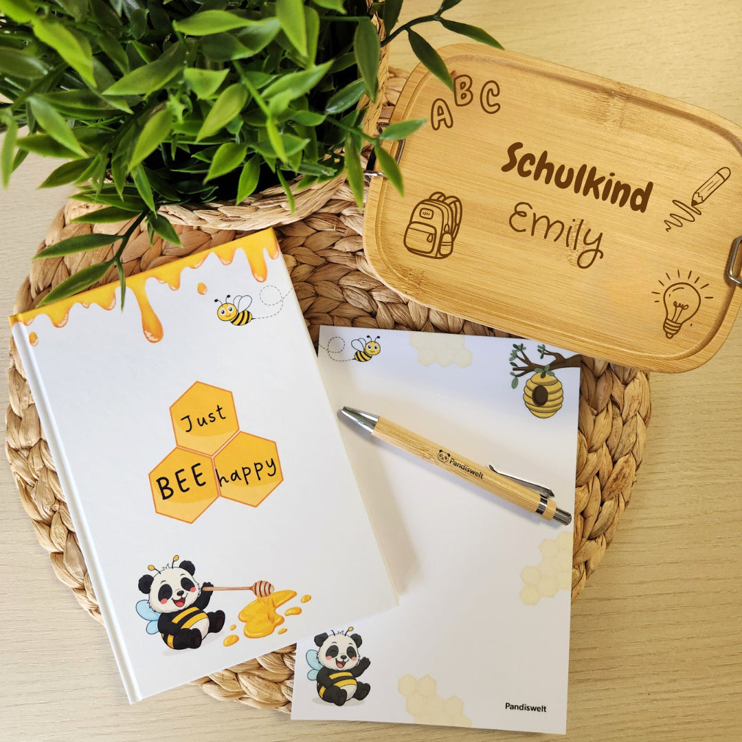 Personalisierte Brotdose mit Namensgravur "Schulkind Emily" neben Notizbuch und Notizblock im Panda-Bienen-Design für die Einschulung