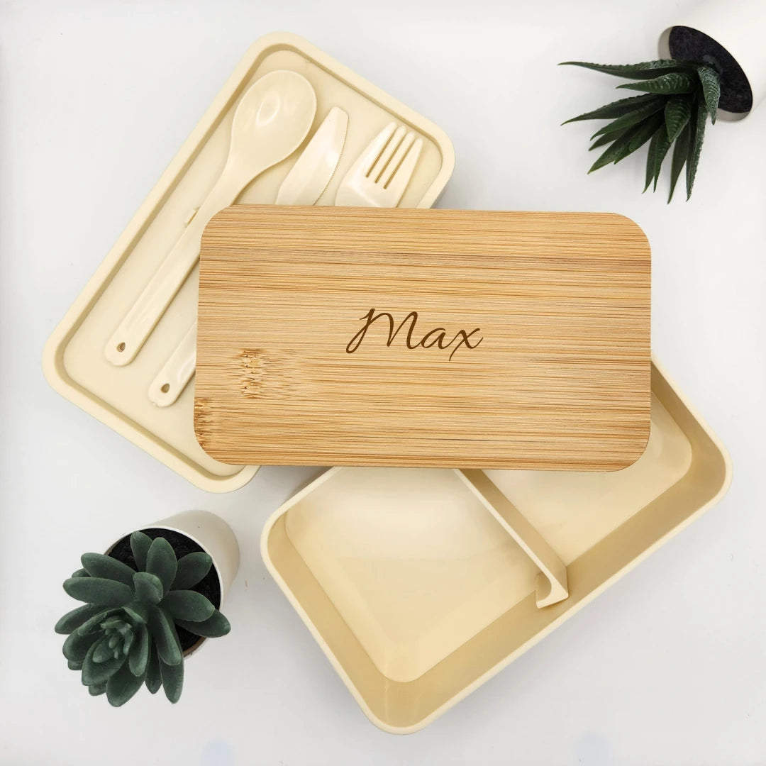 Geöffnete beige Brotdose mit Bambusdeckel und Gravur Max, daneben das Besteckfach mit Löffel, Messer und Gabel