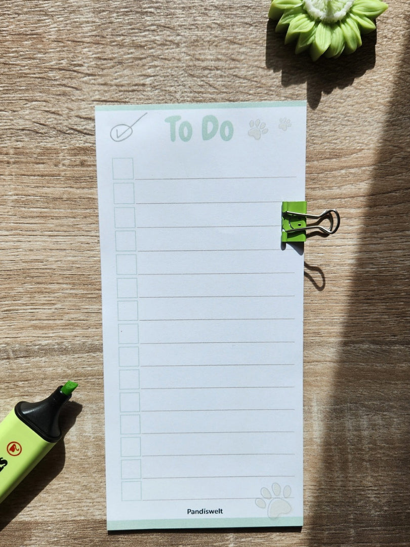 Ein schmaler Checklisten-Block mit 10 Blatt zum strukturierten Abhaken von Aufgaben; zeigt das cleane „To Do“ Design mit grünem Metall-Clip und Pfoten-Detail in natürlichem Licht auf einer Holzoberfläche