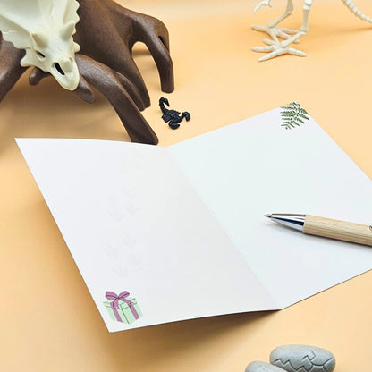 Die aufgeschlagene Innenseite der Dino-Klappkarte bietet viel Platz für persönliche Wünsche, dekoriert mit kleinen Farn- und Geschenk-Illustrationen