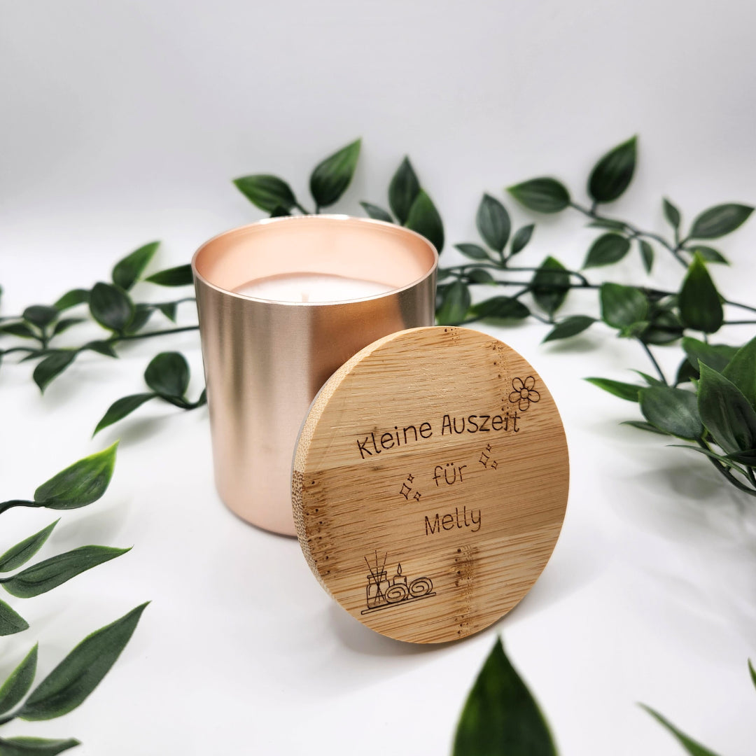 Detailaufnahme der personalisierten Kerze in Rosegold: Der Bambusdeckel zeigt die Lasergravur „Kleine Auszeit für Melly“ mit dekorativen Spa-Symbolen wie Duftstäbchen und Blüten