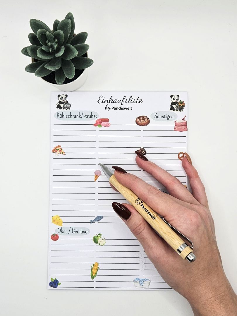 Eine Hand schreibt auf die Panda-Einkaufsliste; zeigt das strukturierte Design und die handliche Handhabung des Blocks für eine effiziente Haushaltsplanung und Vorratsverwaltung