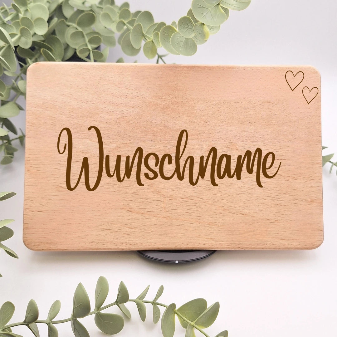 Frühstücksbrett aus Buchenholz mit der Gravur Wunschname in geschwungener Schreibschrift und zwei Herzen in der oberen Ecke, umgeben von Eukalyptuszweigen