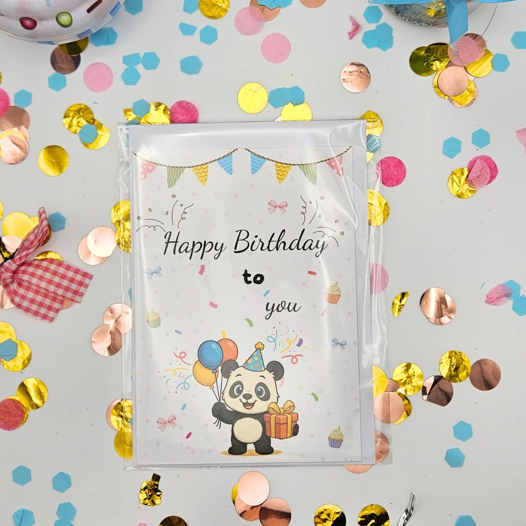 Die Panda-Glückwunschkarte inklusive passendem Briefumschlag, sicher verpackt in einer Klarsichthülle (Polybag), flach liegend auf festlichem Konfetti-Hintergrund
