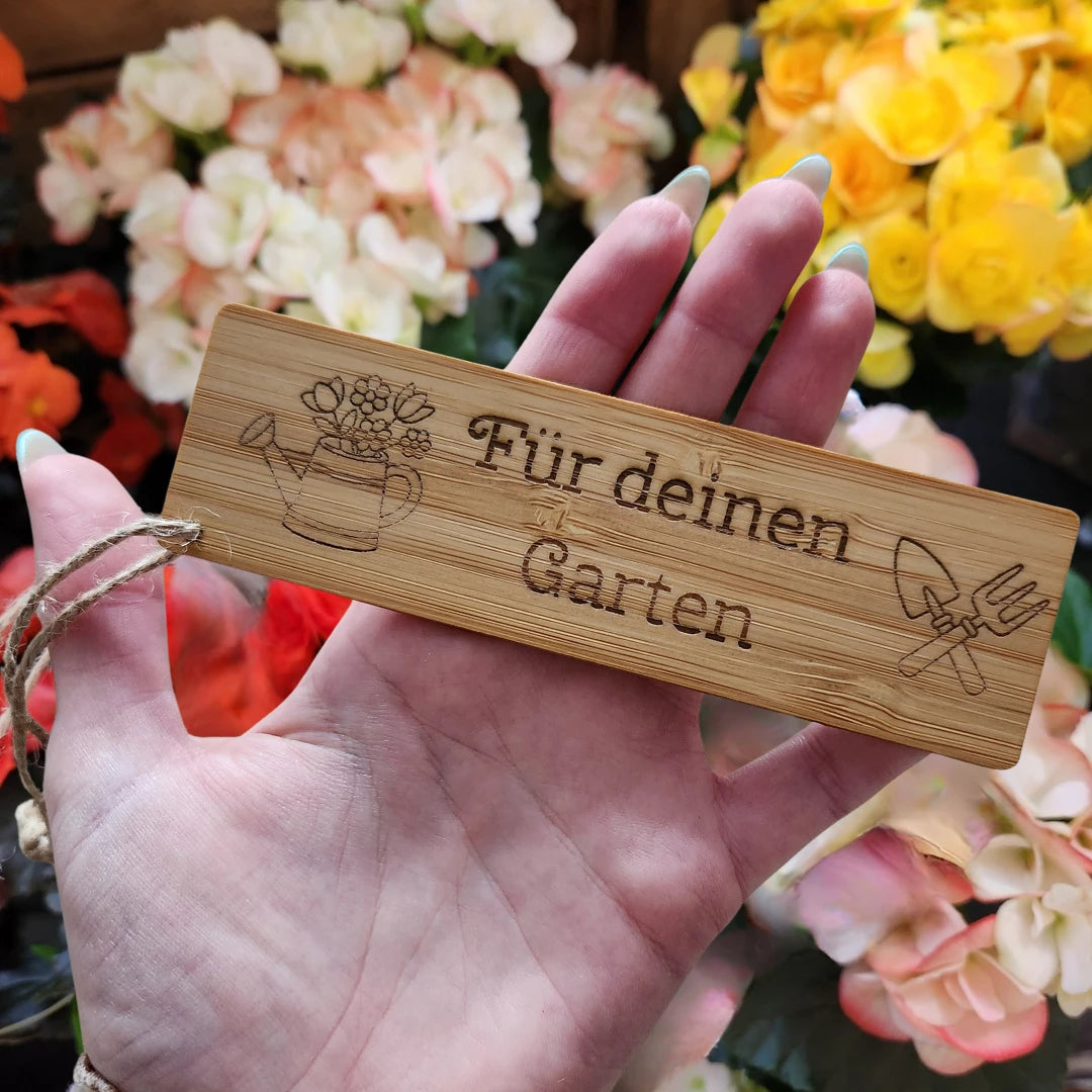 Bambus-Geschenkanhänger mit der Gravur Für deinen Garten, einer Gießkanne mit Blumen und gekreuztem Gartenwerkzeug, mit Juteschnur in einer Hand gehalten