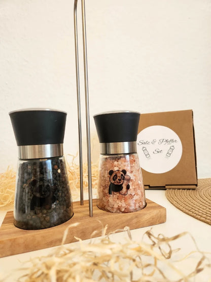 Komplettes Gewürz-Set von Pandiswelt: Salz- und Pfeffermühle inklusive Olivenholz-Halterung, befüllt mit schwarzem Pfeffer und rosa Himalaya-Salz; dekorativ angerichtet mit Geschenkbox im rustikalen Stil