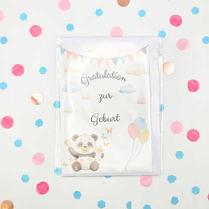 Frontansicht der Glückwunschkarte zur Geburt im Format A6 mit Baby-Panda, Heißluftballons und Wolken; verpackt in Schutzhülle inklusive Umschlag auf buntem Konfetti-Hintergrund