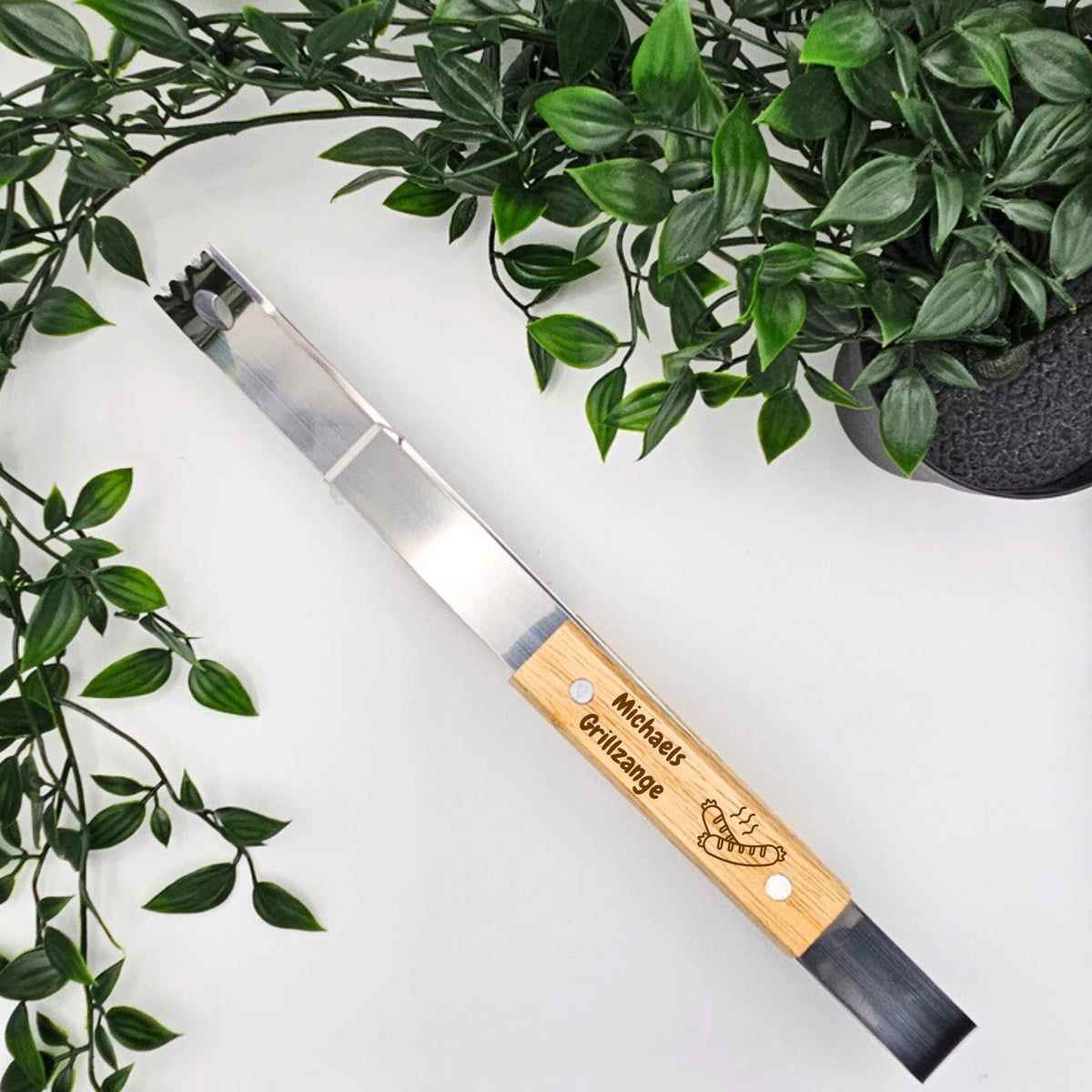 Grillzange personalisiert mit "Michaels Grillzange" und einem Bratwurst Motiv aus Holz und Edelstahl.