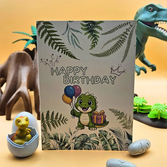 Detailansicht der Glückwunschkarte mit einem niedlichen grünen Dinosaurier, bunten Luftballons und Geschenk, umrahmt von Farnblättern im Jungle-Design