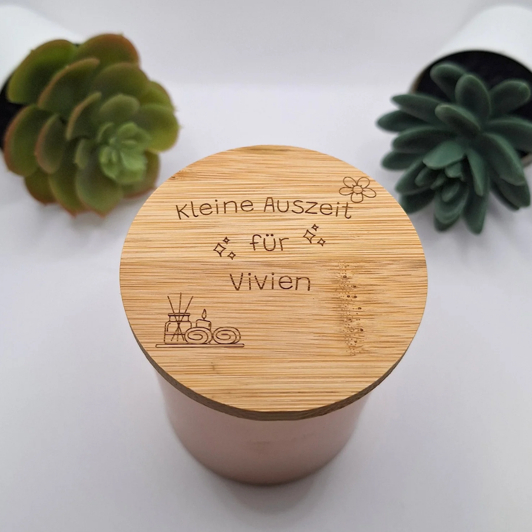 Personalisierte Duftkerze in Rosegold mit der beispielhaften Deckel-Gravur „Kleine Auszeit für Vivien“, modern inszeniert zwischen zwei grünen Sukkulenten-Pflanzen