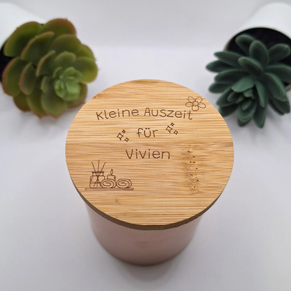 Personalisierte Duftkerze in Rosegold mit der beispielhaften Deckel-Gravur „Kleine Auszeit für Vivien“, modern inszeniert zwischen zwei grünen Sukkulenten-Pflanzen