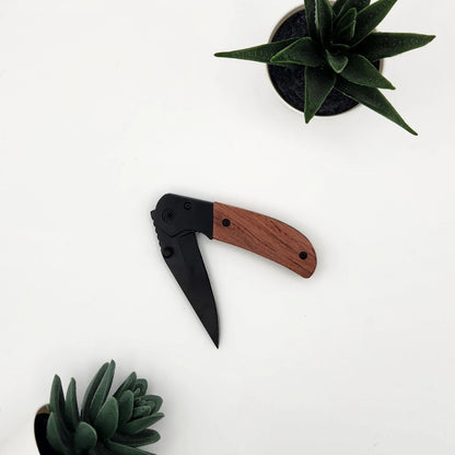 Halb geöffnetes Klappmesser mit schwarzer Klinge und rotbraunem Holzgriff von oben fotografiert