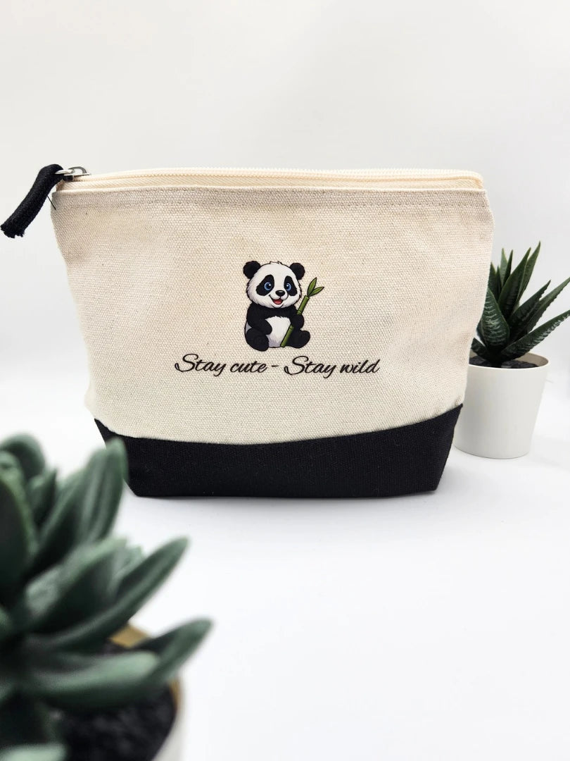 Nachhaltige Kosmetiktasche aus cremefarbener Baumwolle mit schwarzem Boden und Panda-Motiv; der Aufdruck zeigt den Schriftzug „Stay cute - Stay wild“ in moderner Typografie, präsentiert mit grünen Sukkulenten