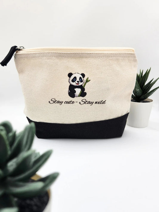 Nachhaltige Kosmetiktasche aus cremefarbener Baumwolle mit schwarzem Boden und Panda-Motiv; der Aufdruck zeigt den Schriftzug „Stay cute - Stay wild“ in moderner Typografie, präsentiert mit grünen Sukkulenten
