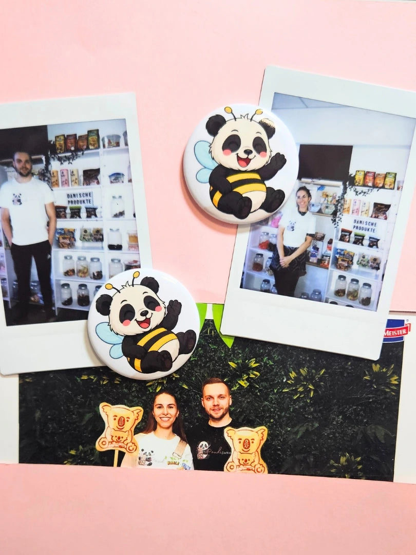 Ein süßer Panda-Magnet im Bienen-Kostüm fixiert Polaroid-Fotos auf einem rosa Untergrund; zeigt die Nutzung als dekorativer Fotohalter für Kühlschrank oder Magnettafel, ideal als kleines Geschenk