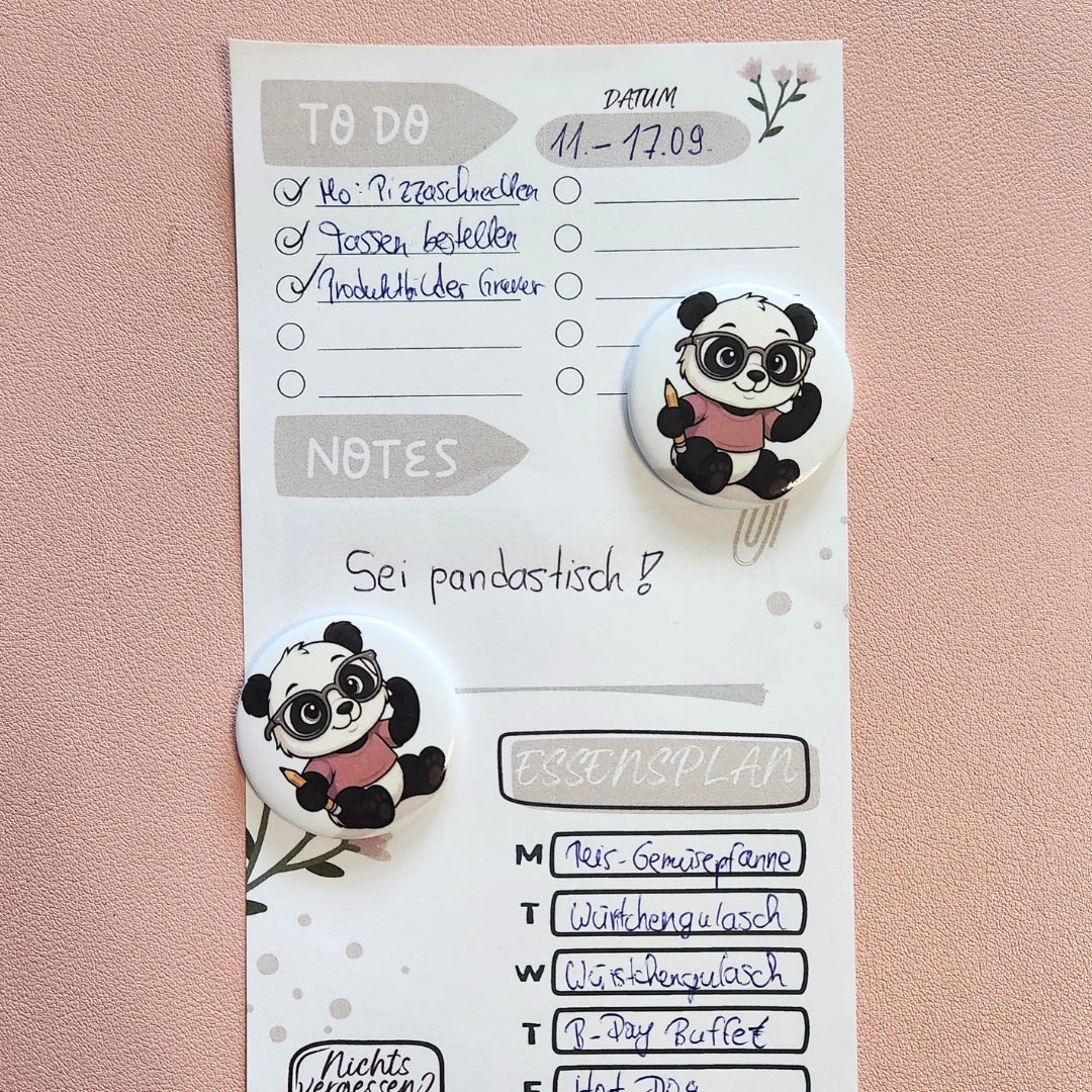 Ein Panda-Magnet mit Brille und Stift fixiert einen beispielhaften Essensplan und eine To-Do-Liste; ideal zur Organisation von Terminen und Wochenplänen am Kühlschrank oder einer Magnettafel