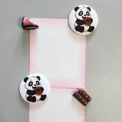 Ein runder Magnet (3,8 cm) mit einem naschenden Panda und Schokoladen-Donut; gezeigt als Anwendungsbeispiel zum Befestigen eines rosafarbenen Notizzettels an einer grauen Magnetwand oder einem Kühlschrank
