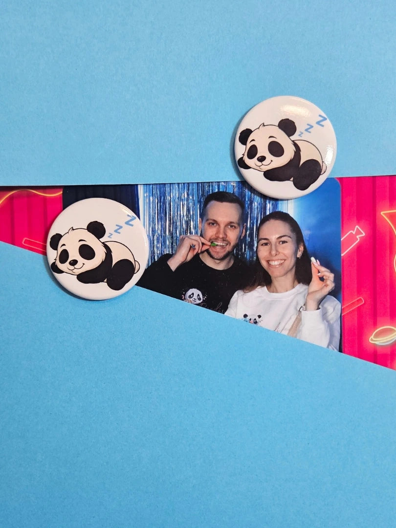Zwei runde Magnete mit niedlichem schlafenden Panda-Motiv fixieren ein persönliches Foto auf einem blauen Untergrund; zeigt die praktische Anwendung als Fotohalter für den Kühlschrank oder die Magnetwand