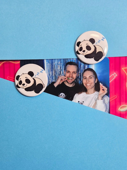 Zwei runde Magnete mit niedlichem schlafenden Panda-Motiv fixieren ein persönliches Foto auf einem blauen Untergrund; zeigt die praktische Anwendung als Fotohalter für den Kühlschrank oder die Magnetwand