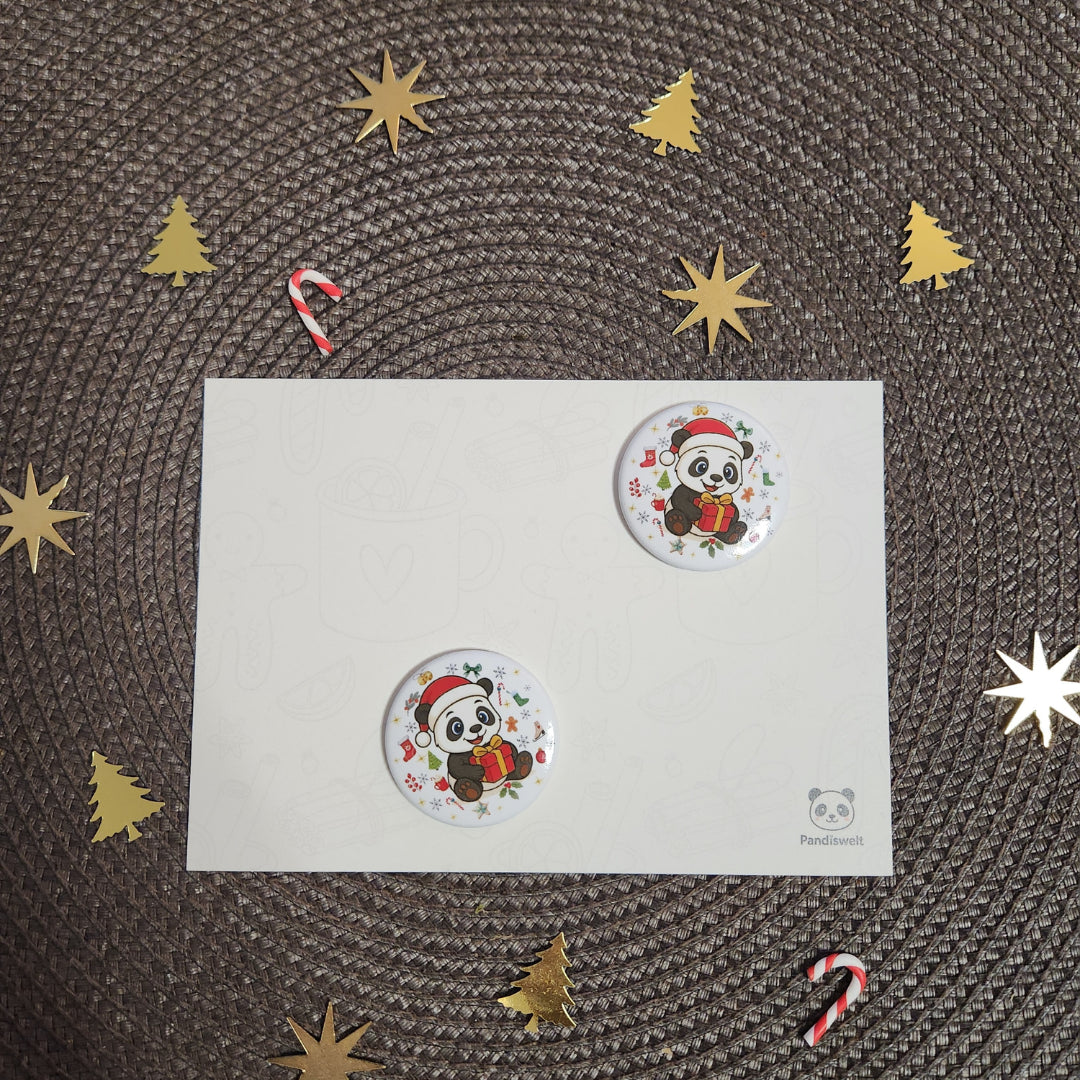 Runder Weihnachts-Magnet (Ø 3,8 cm) mit einem niedlichen Panda-Motiv in Nikolausmütze und mit Geschenk; das Design wird auf einer festlichen Karte präsentiert, umgeben von weihnachtlichen Elementen wie goldenen Sternen und Zuckerstangen
