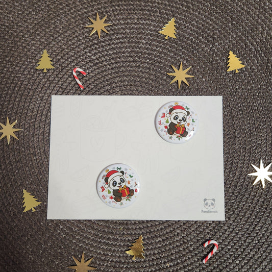 Runder Weihnachts-Magnet (Ø 3,8 cm) mit einem niedlichen Panda-Motiv in Nikolausmütze und mit Geschenk; das Design wird auf einer festlichen Karte präsentiert, umgeben von weihnachtlichen Elementen wie goldenen Sternen und Zuckerstangen