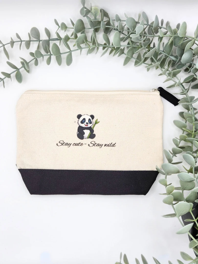 Ästhetische Draufsicht der Panda-Tasche aus robustem Canvas; die Baumwolltasche mit Reißverschluss und schwarzem Stoff-Detail ist dekorativ unter Eukalyptus-Zweigen platziert, ideal als Geschenk für Panda-Fans
