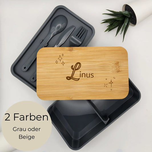 Graue Lunchbox mit Bambusdeckel und Gravur Linus mit Sternen, daneben das Besteckfach mit Löffel, Messer und Gabel
