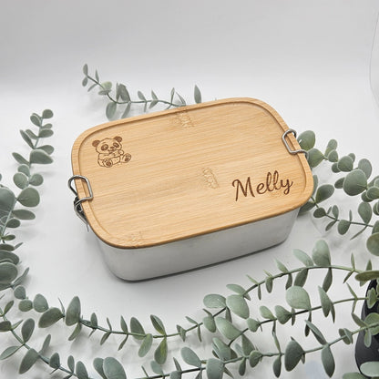 Ästhetisches Produktbild der personalisierten Edelstahl-Brotdose, dekorativ umrahmt von Eukalyptus-Zweigen; eine nachhaltige und persönliche Geschenkidee für Panda-Fans