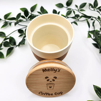 Nahaufnahme des geöffneten Mehrweg-Kaffeebechers mit abgenommenem Bambusdeckel; sichtbar ist die detailreiche Lasergravur „Melly's Coffee Cup“ vor einem natürlichen Blätter-Hintergrund