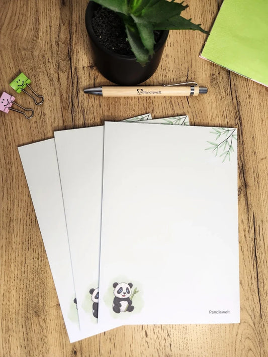 Ansicht des A5 Notizblocks von Pandiswelt mit niedlichem Panda-Bambus-Design; dekorativ präsentiert auf einem Holztisch mit passendem Bambuskugelschreiber und grünen Büro-Clips