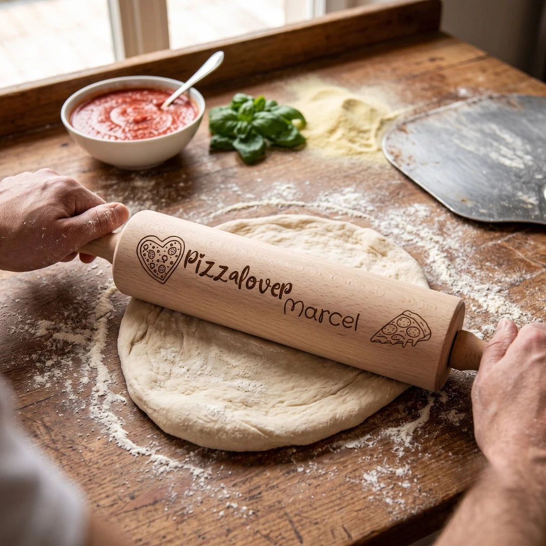 Zwei Hände rollen mit dem gravierten Nudelholz einen runden Pizzateig auf einer bemehlten Holzplatte aus