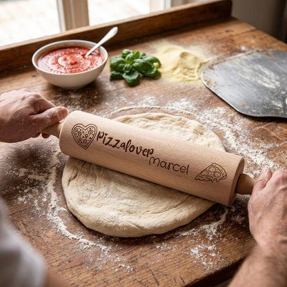 Zwei Hände rollen mit dem gravierten Nudelholz einen runden Pizzateig auf einer bemehlten Holzplatte aus