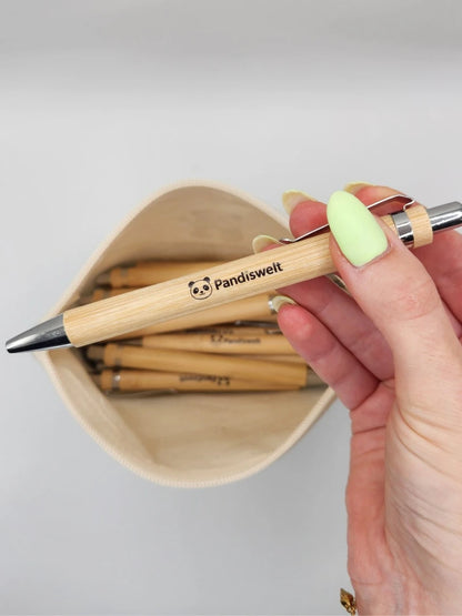 Detailaufnahme eines ökologischen Kugelschreibers aus Bambus mit silbernem Clip; gehalten über einem gefüllten Federmäppchen, zeigt die natürliche Holzmaserung und das präzise Branding