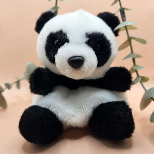 Niedliches, sitzendes Panda-Kuscheltier (13 cm) vor einem neutralen Hintergrund mit dekorativen Eukalyptus-Zweigen; flauschiges Pandabär-Stofftier ideal als kleines Geschenk oder Glücksbringer