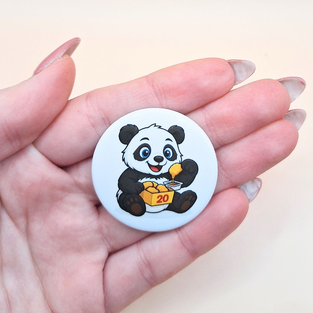 Größenvergleich des runden Panda-Magnets: Die Illustration mit dem Panda, der Chicken Nuggets isst, wird in der Hand präsentiert, um die handliche Größe von 3,8 cm Durchmesser für Kühlschrank oder Magnetwand zu verdeutlichen