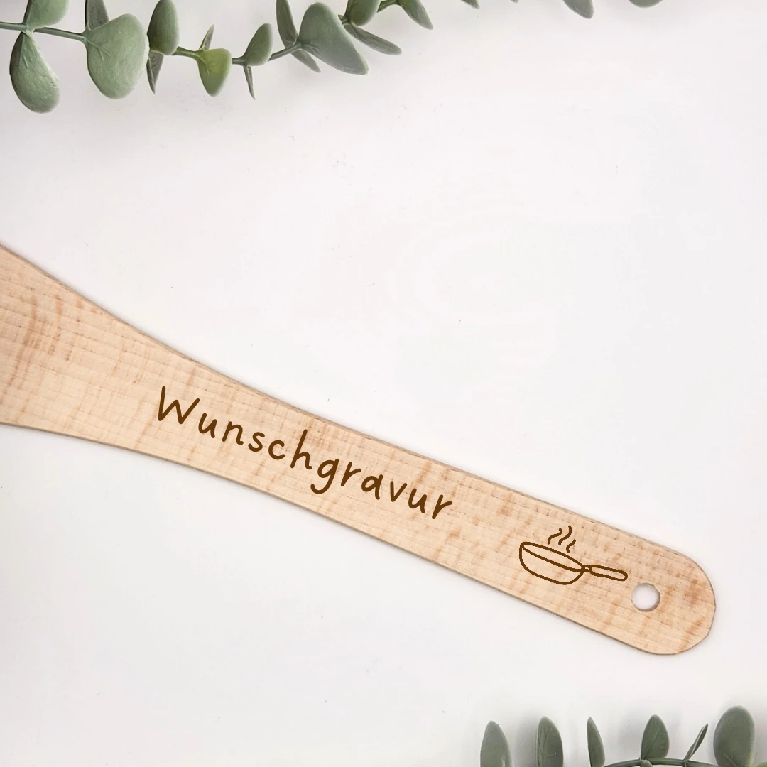 Nahaufnahme des Holzwenders mit gravierter dampfender Pfanne, dem Platzhalter Wunschgravur und dem Loch zum Aufhängen