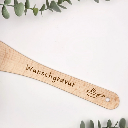 Nahaufnahme des Holzwenders mit gravierter dampfender Pfanne, dem Platzhalter Wunschgravur und dem Loch zum Aufhängen