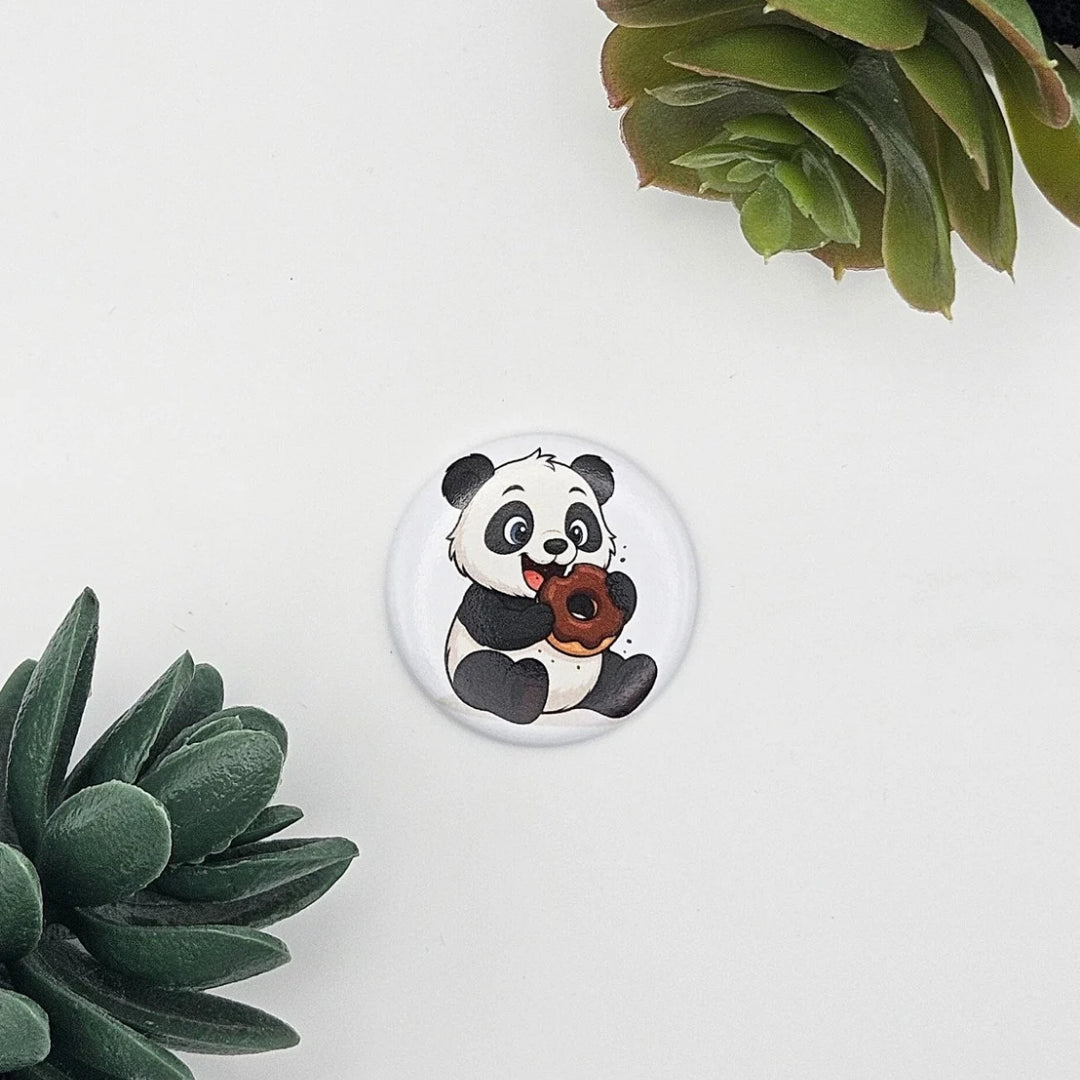 Detailansicht eines einzelnen runden Magnets mit Panda-Illustration und Donut; ästhetisch präsentiert auf weißem Hintergrund zwischen grünen Sukkulenten-Blättern