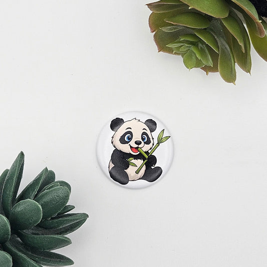 Einzelner runder Kühlschrankmagnet (Ø 3,8 cm) mit einer Illustration eines Pandas, der einen Bambusstab hält; modern inszeniert auf weißem Grund zwischen grünen Sukkulenten-Blättern