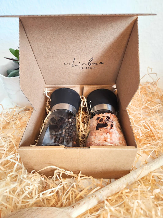 Geöffnete Geschenkbox mit befüllten Salz- und Pfeffermühlen, gebettet auf natürlicher Holzwolle; der Innendeckel trägt den Schriftzug „Mit Liebe gemacht“, zeigt den hochwertigen Lieferumfang inklusive Füllung