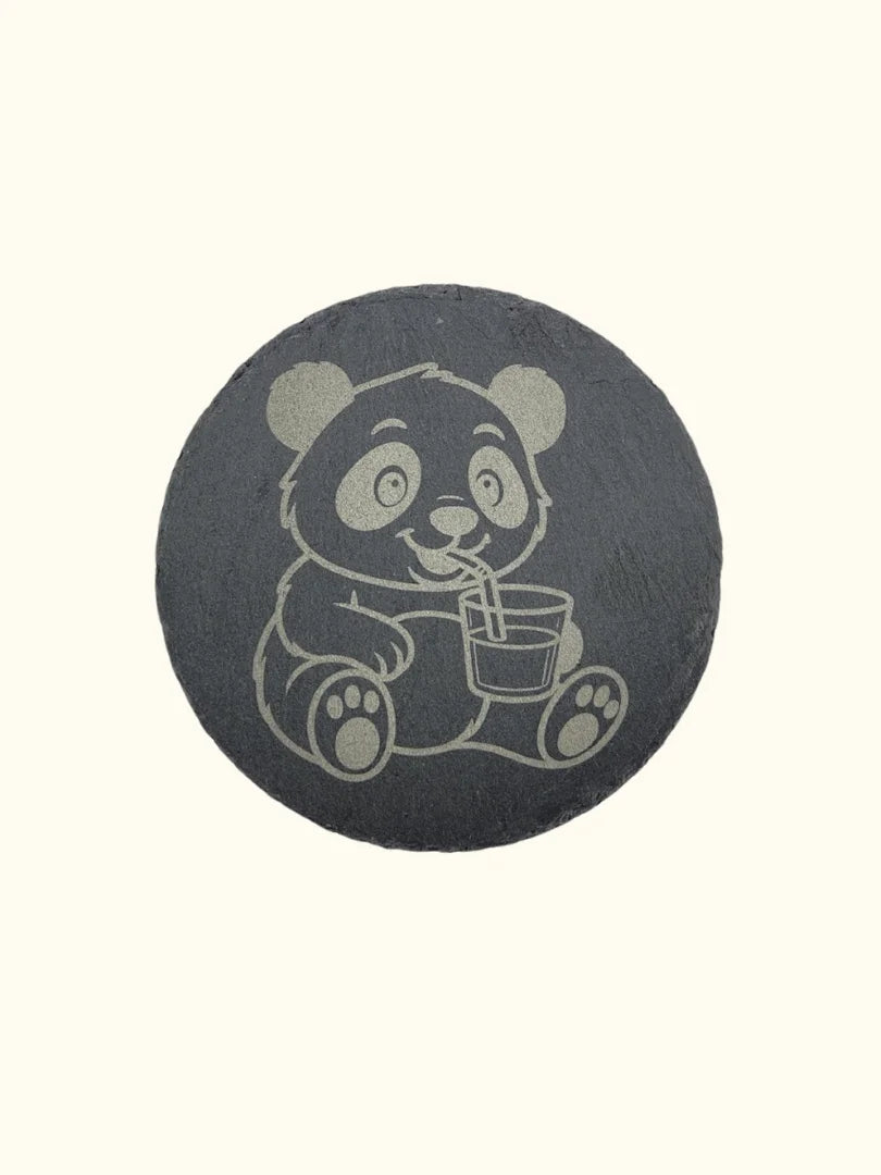 Runder Untersetzer aus dunklem Naturschiefer (Ø 10 cm) mit einer hochwertigen Lasergravur eines Pandas, der mit einem Strohhalm aus einem Glas trinkt; elegante Tischdeko mit rustikaler Naturkante