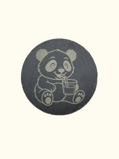 Runder Untersetzer aus dunklem Naturschiefer (Ø 10 cm) mit einer hochwertigen Lasergravur eines Pandas, der mit einem Strohhalm aus einem Glas trinkt; elegante Tischdeko mit rustikaler Naturkante