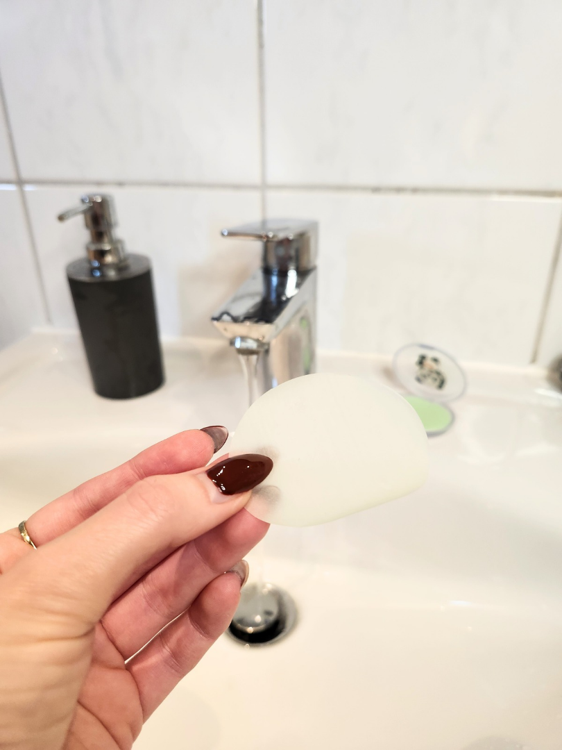 Ein einzelnes, hauchdünnes Seifenblatt wird über einem Waschbecken gehalten; zeigt die praktische Handhabung der Reiseseife für hygienisches Händewaschen auf Reisen