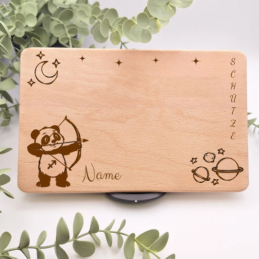 Sternzeichenbrett personalisiert mit Namen und einem Motiv passend zum Sternzeichen. Beispielsweise Schütze mit einem Panda als Schütze, dazu einen Halbmond mit Sternen und Weltallkugeln.