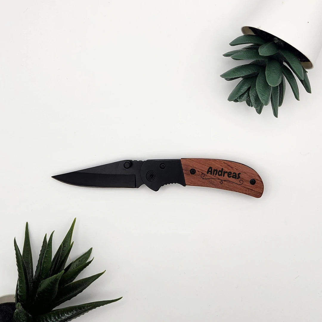 Aufgeklapptes Taschenmesser mit schwarzer Klinge und der Namensgravur Andreas auf dem Holzgriff