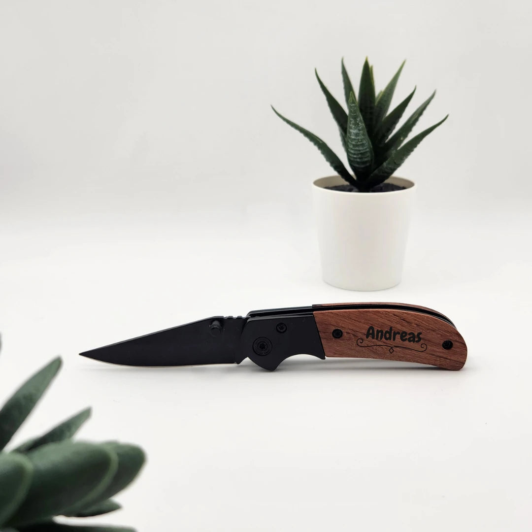 Taschenmesser mit Holzgriff und Gravur Andreas, aufgeklappt neben einer Sukkulente im weißen Topf