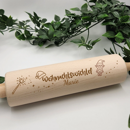 Teigroller aus Buchenholz mit der Gravur Weihnachtswichtel und dem Namen Marie, daneben ein Wichtel, eine Zipfelmütze, ein Zauberstab und Sternenstaub